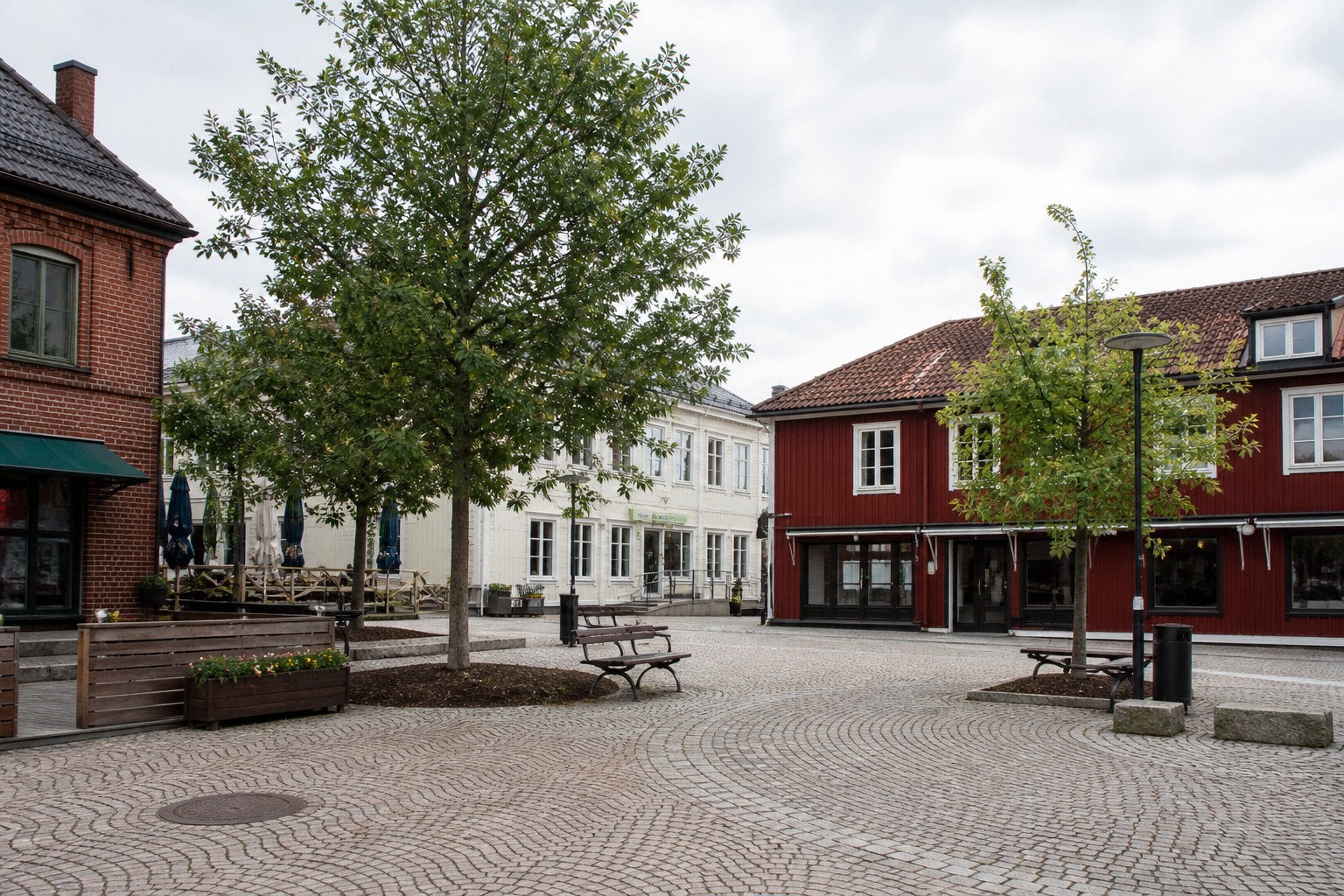 Ett stilla torg bland träd och tegel, i mänsklig skala.